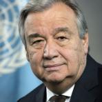 A portrait of a distinguished gentleman with a suit and tie, against a backdrop featuring the united nations emblem.