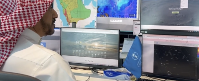 A man in traditional Middle Eastern attire monitors weather data and maps on multiple computer screens at a meteorological center.
