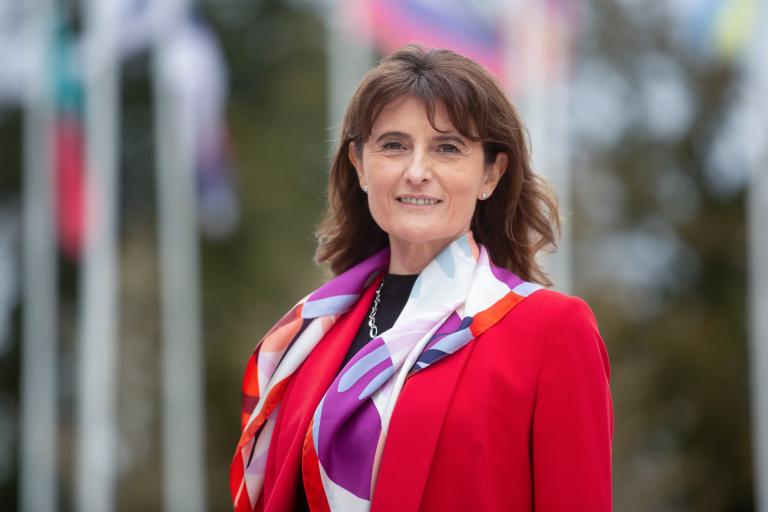 A woman in a red jacket standing in front of flags.
