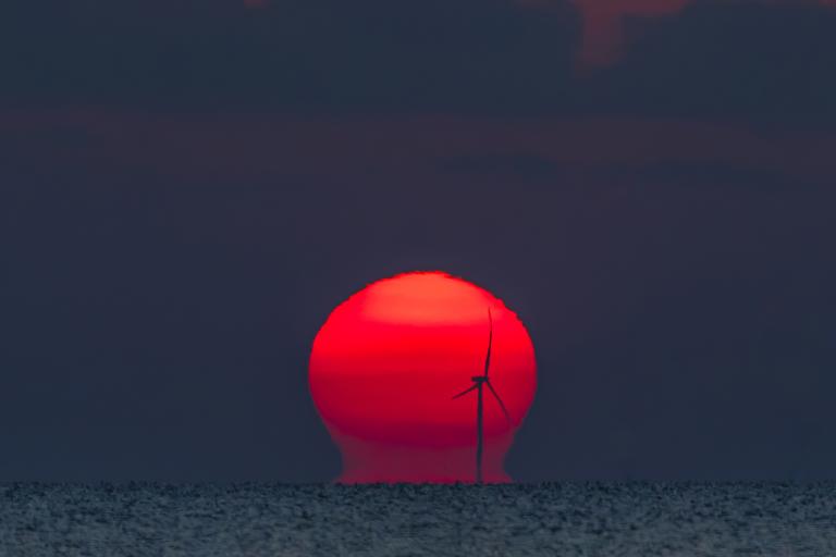A red sunset with a wind turbine in the background.