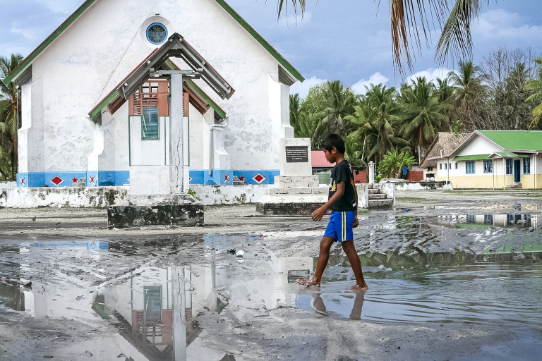 A boy walks through a puddle in front of a church.