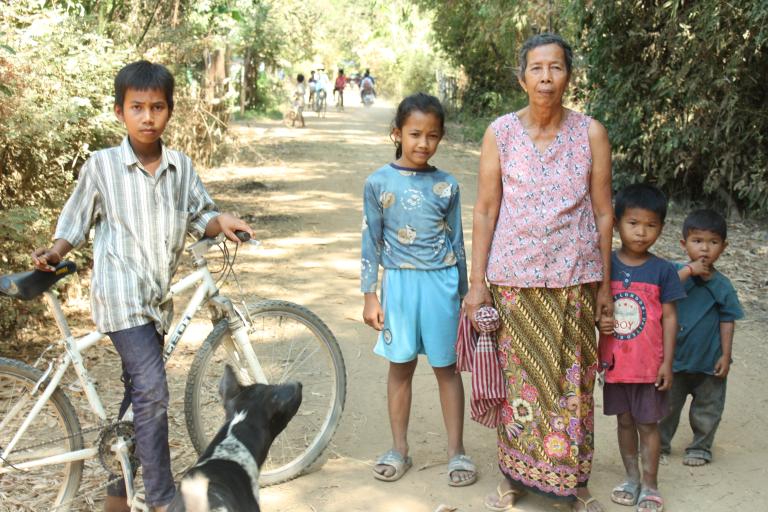 A group of people standing next to a bicycle on a dirt road.