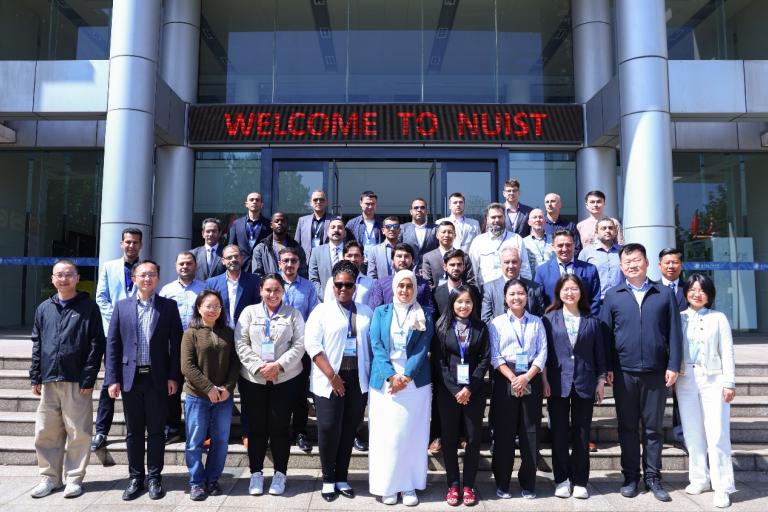A group of people stands in front of a building with a sign that reads "Welcome to NUIST." They are posing for a group photo on steps outside the entrance.