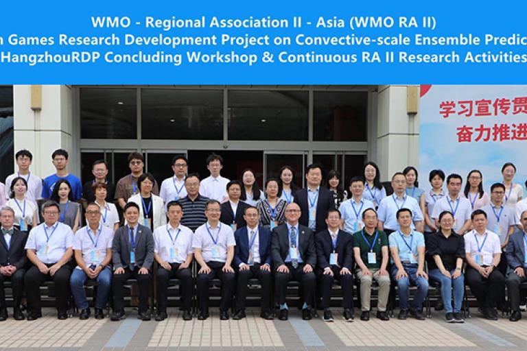 Group photo of conference attendees standing and seated in front of a banner for the 19th Hangzhou Asian Games research project and related workshops.