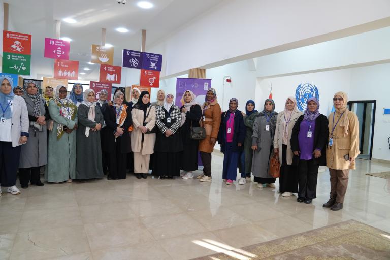 A group of people stands together indoors in front of colorful posters. Some are wearing badges and headscarves.
