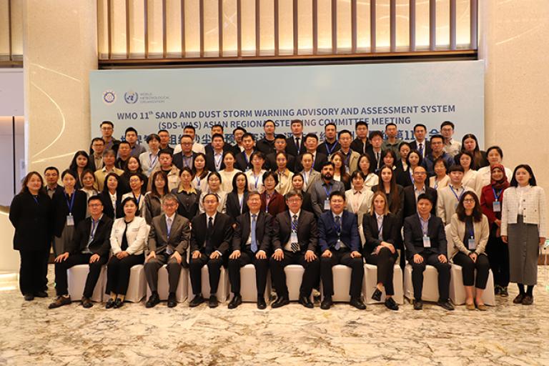 A large group of people in business attire pose for a group photo at the WMO 11th Sand and Dust Storm Warning Advisory and Assessment System meeting.