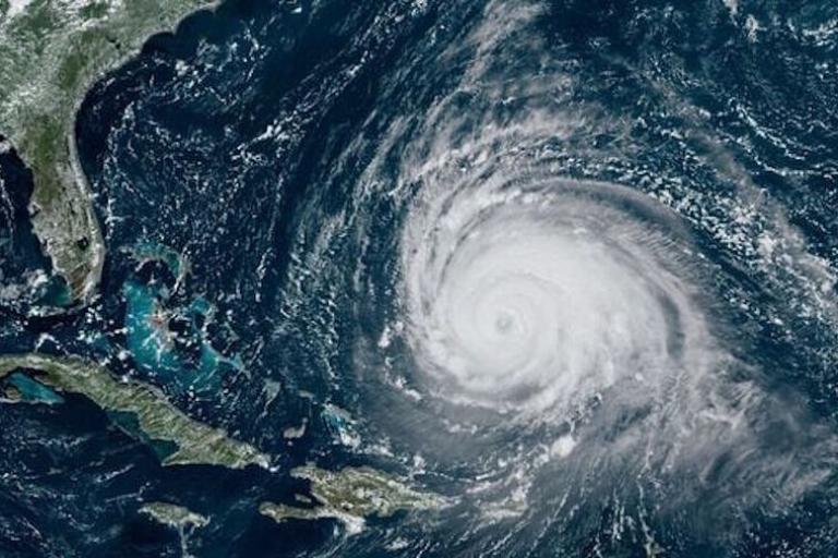 Satellite image showing a large hurricane with a well-defined eye over the Atlantic Ocean, approaching the southeastern coast of the United States and the Caribbean.