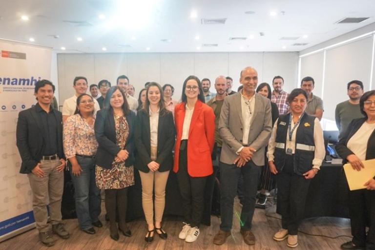 A group of people pose for a photo in a conference room, standing in front of a Senamhi banner and a projection screen.