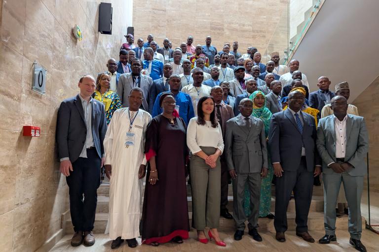 A large group of people in formal attire pose for a photo on a staircase inside a modern building.