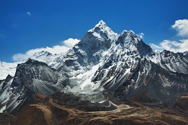 Snow-capped mountain peaks rise under a clear blue sky, with rocky slopes and patches of brown terrain in the foreground.