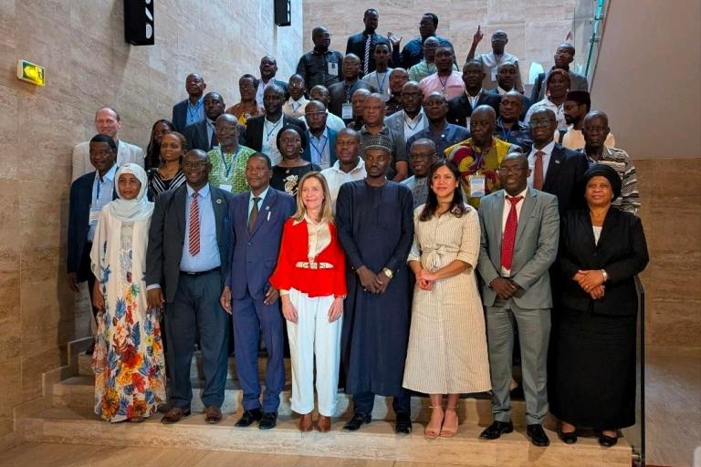 A large group of men and women in formal attire stand on stairs posing for a group photo indoors.