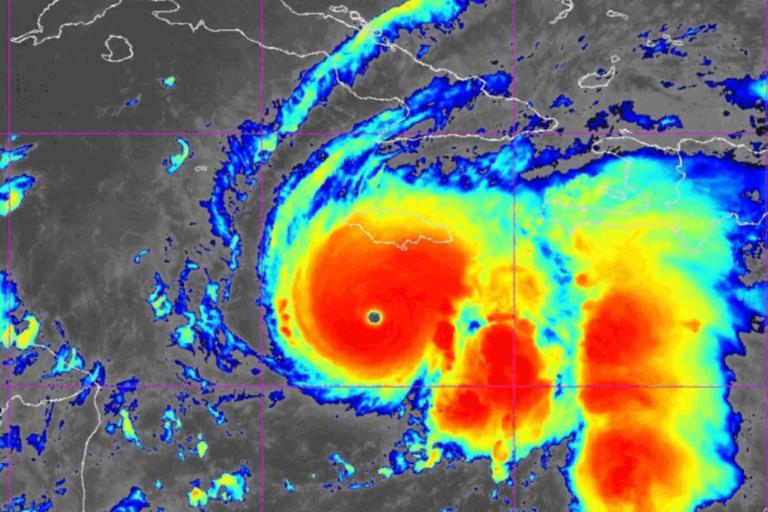 Satellite image shows a large hurricane with a clear eye, displaying intense red and yellow cloud bands indicating strong storm activity approaching land.