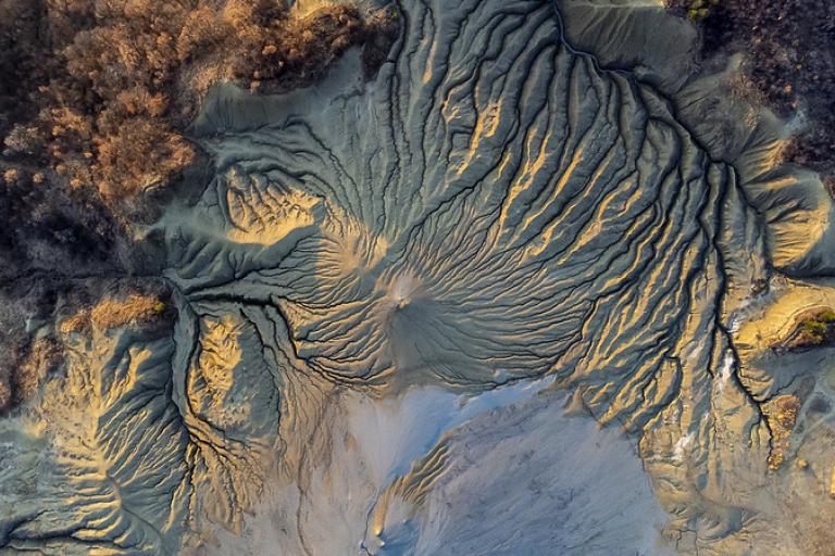 Aerial view of mud cracks and channels in a dry, barren landscape with some vegetation on the edges.