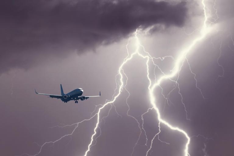 A commercial airplane flies near a large lightning strike in a dark, cloudy sky.