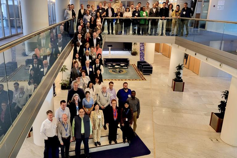 A large group of people poses for a group photo in a modern building with two floors, some standing on the upper level and others on the ground floor.