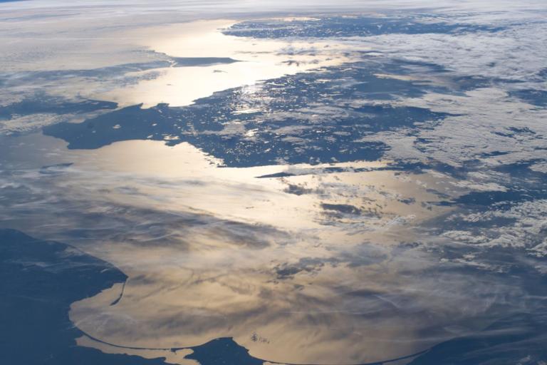 A view of northwestern Europe from space, with land, clouds, and sunlight reflecting off the surrounding sea.