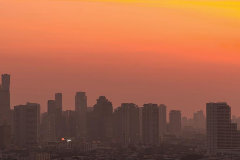 Silhouetted city skyline with numerous high-rise buildings under an orange and yellow sunset sky.