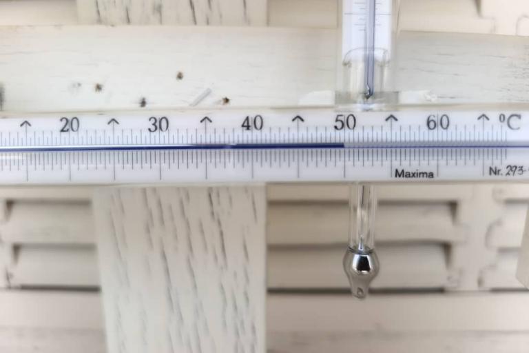 A close-up of a thermometer showing a temperature reading of approximately 49 degrees Celsius against a white wooden background.