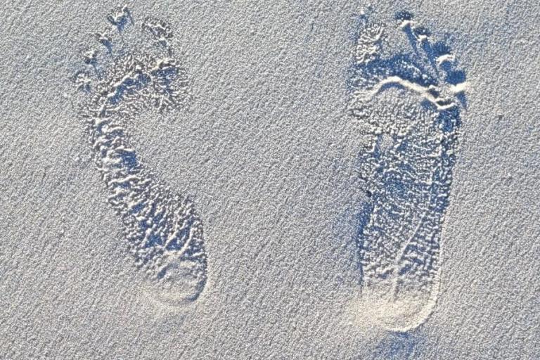 Two barefoot footprints are pressed into smooth, pale sand, with visible toe and heel marks.