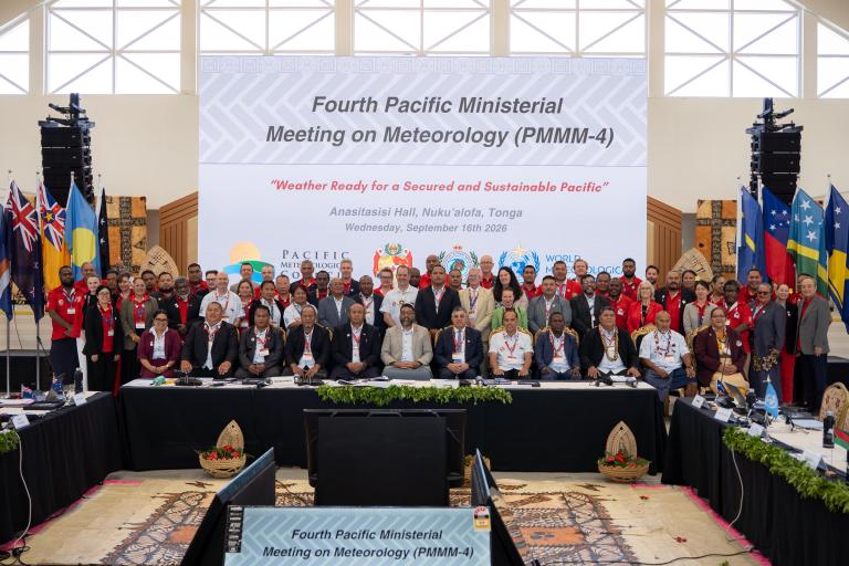 A large group of people poses for a photo at the Fourth Pacific Ministerial Meeting on Meteorology, with national flags and a conference banner in the background.