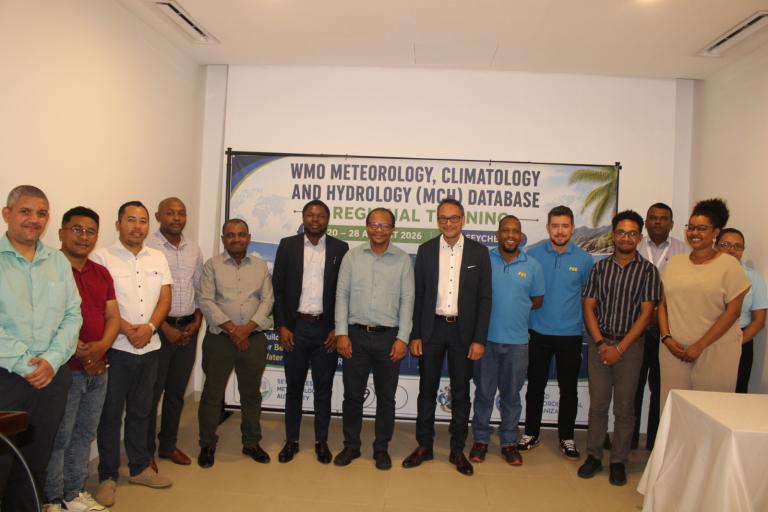 A group of fifteen people standing in front of a banner for a WMO Meteorology, Climatology and Hydrology database training session.