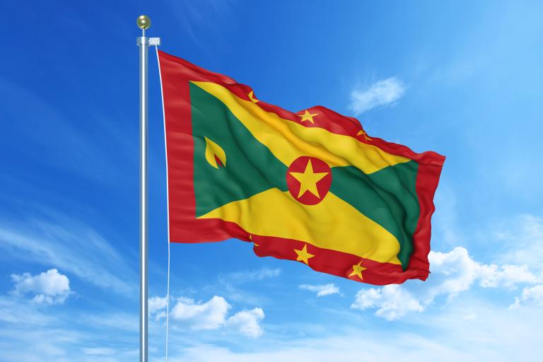 The national flag of Grenada flying on a flagpole against a blue sky.