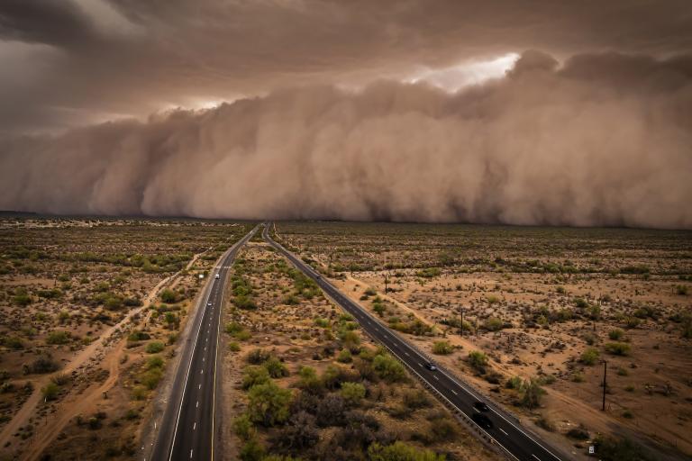 A massive dust storm approaching a highway running through a desert landscape.