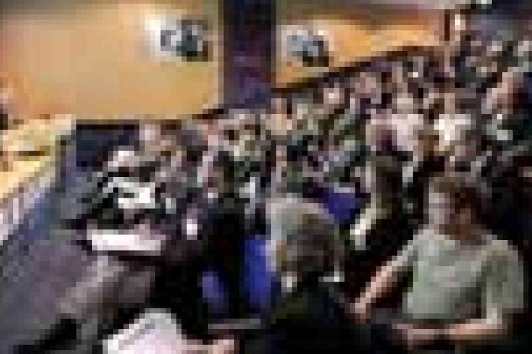 A large audience sits in rows facing a stage or panel in a conference or lecture hall.