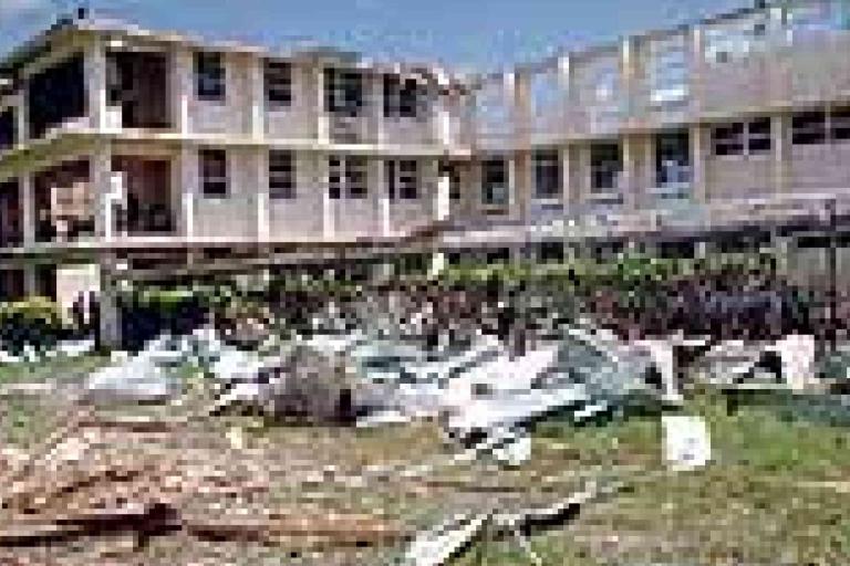 A two-story building with significant exterior damage, debris, and scattered materials covering the surrounding ground.