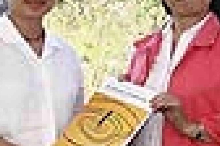 Two people standing outdoors holding a yellow book with a maze design on the cover, both facing the camera.