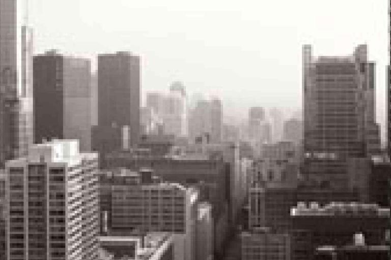 Black and white photo of a city skyline with tall buildings and skyscrapers under a hazy sky.