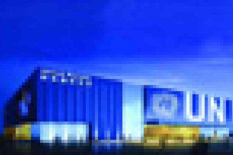 A modern building with a blue exterior and large white "UNI" letters on the facade, shown under a deep blue sky.