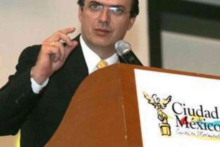 A man in a suit speaks at a podium labeled "Ciudad de México" with a microphone, making a gesture with his hand.