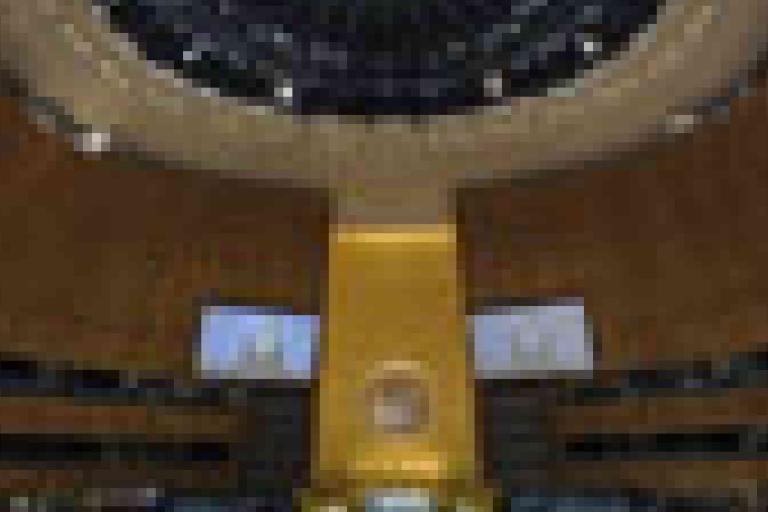 A large, round auditorium with wood-paneled walls, a central podium, and two projection screens, beneath a domed ceiling.