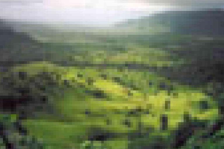 A blurry, pixelated image of a green valley surrounded by hills, with sunlight filtering through clouds above.