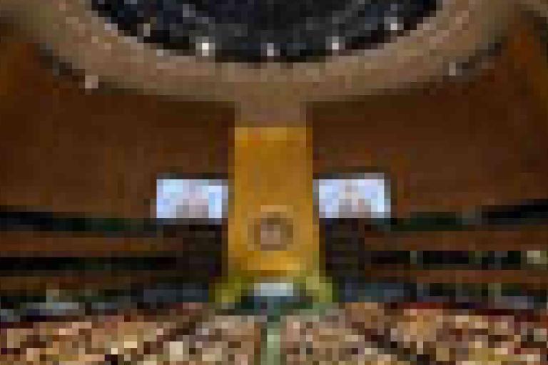 A large assembly hall filled with delegates seated in rows, featuring a central podium and the United Nations emblem on a golden wall.