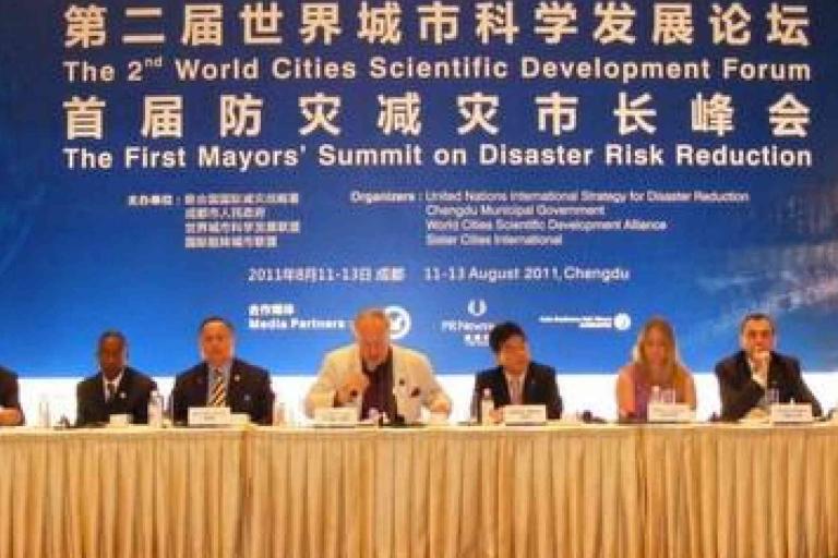 A panel of eight people sits at a conference table onstage under a banner for the First Mayors' Summit on Disaster Risk Reduction, held in Chengdu in August 2011.