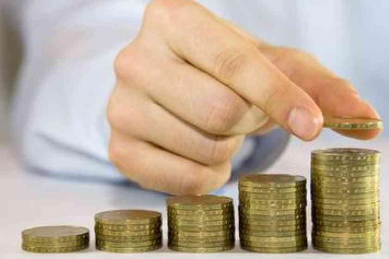 A person stacks coins in ascending order, showing an increasing progression of coin piles on a table.
