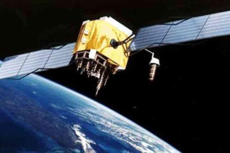 A satellite with solar panels orbits above Earth, with part of the planet and its atmosphere visible below.