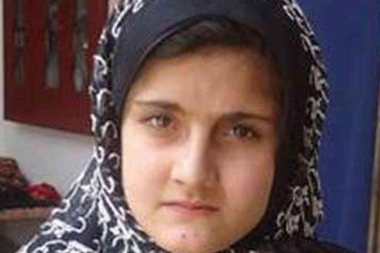 A young girl wearing a patterned black and white headscarf looks directly at the camera with a neutral expression.