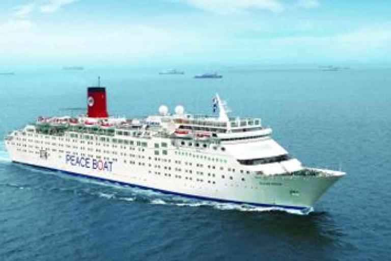 A white cruise ship labeled "Peace Boat" sails on calm blue ocean water under a clear sky, with other ships visible in the distant background.