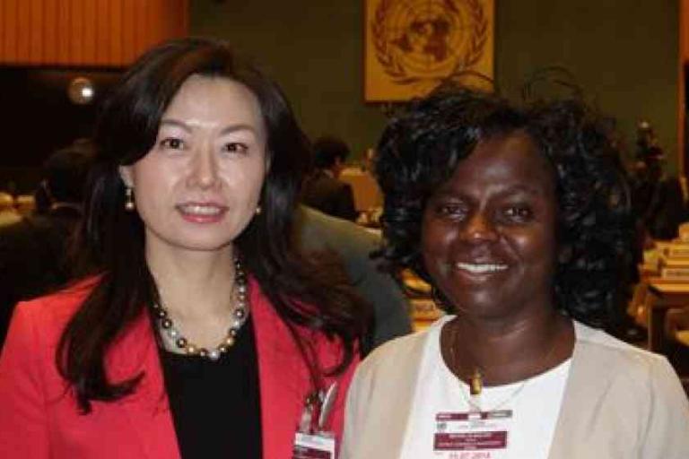 Two women standing together and smiling at an indoor conference with United Nations emblem visible in the background.