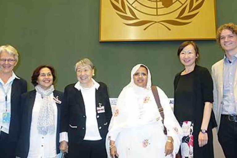 Six people stand together in front of a green wall with a large United Nations emblem, posing for a group photo.