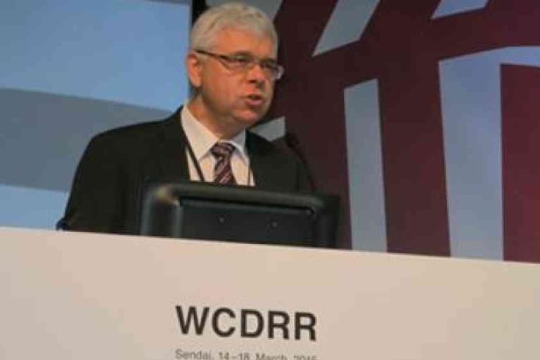 A man in a suit speaks at a podium labeled "WCDRR" during a conference.