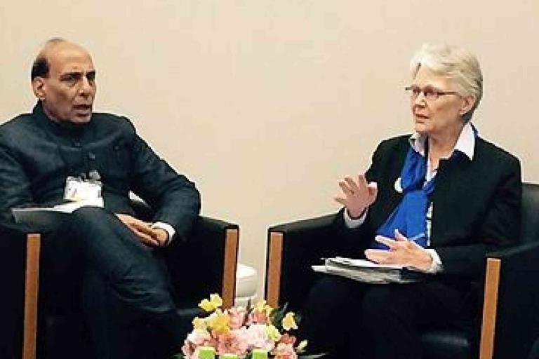 Two people sit in chairs having a conversation indoors, with a small bouquet of flowers on the table between them.