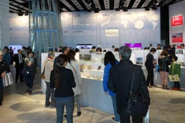 A group of people observe displays and exhibits in a well-lit, modern museum or exhibition space.