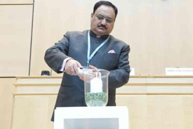 A man in a suit places an object into a glass container filled with green items on a podium in a conference room.