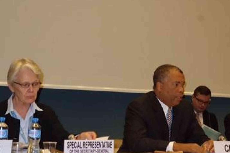 A woman and a man sit at a conference table with nameplates reading "Special Representative" and "Chair," participating in a formal meeting.