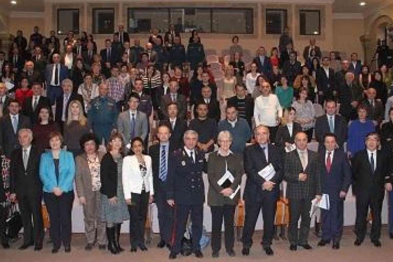 A large group of people, formally dressed, stand and sit in rows inside an auditorium, posing for a group photo.