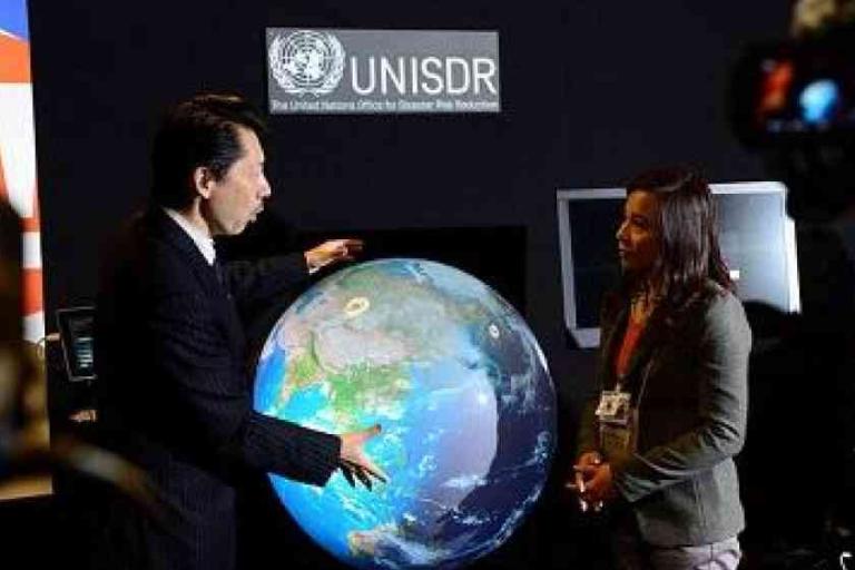 Two people converse in front of a digital globe display at a UNISDR (United Nations Office for Disaster Risk Reduction) event.